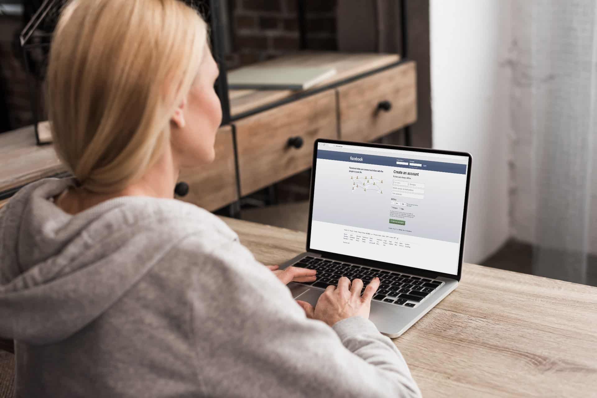 A blonde woman logs into Facebook on her laptop - Facebook location tracking