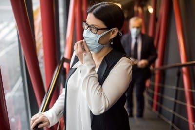 A woman adjusts her face mask while a man in a face mask approaches her in the background - coronavirus restrictions