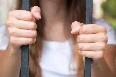 A woman wearing a white shirt holds on to vertical jail cell bars - excessive force