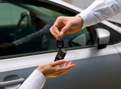 Closeup of a man handing a woman a car key near a silver car - mass layoffs