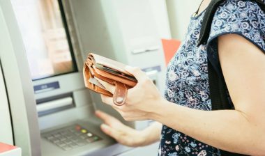 A woman holds a brown wallet in one hand while using the other hand to make selections at an ATM - ATM fees