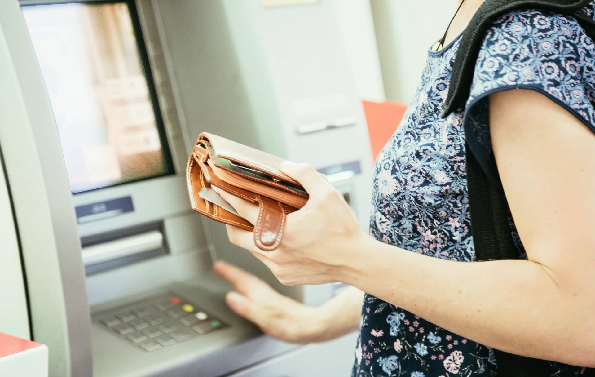 A woman holds a brown wallet in one hand while using the other hand to make selections at an ATM - ATM fees