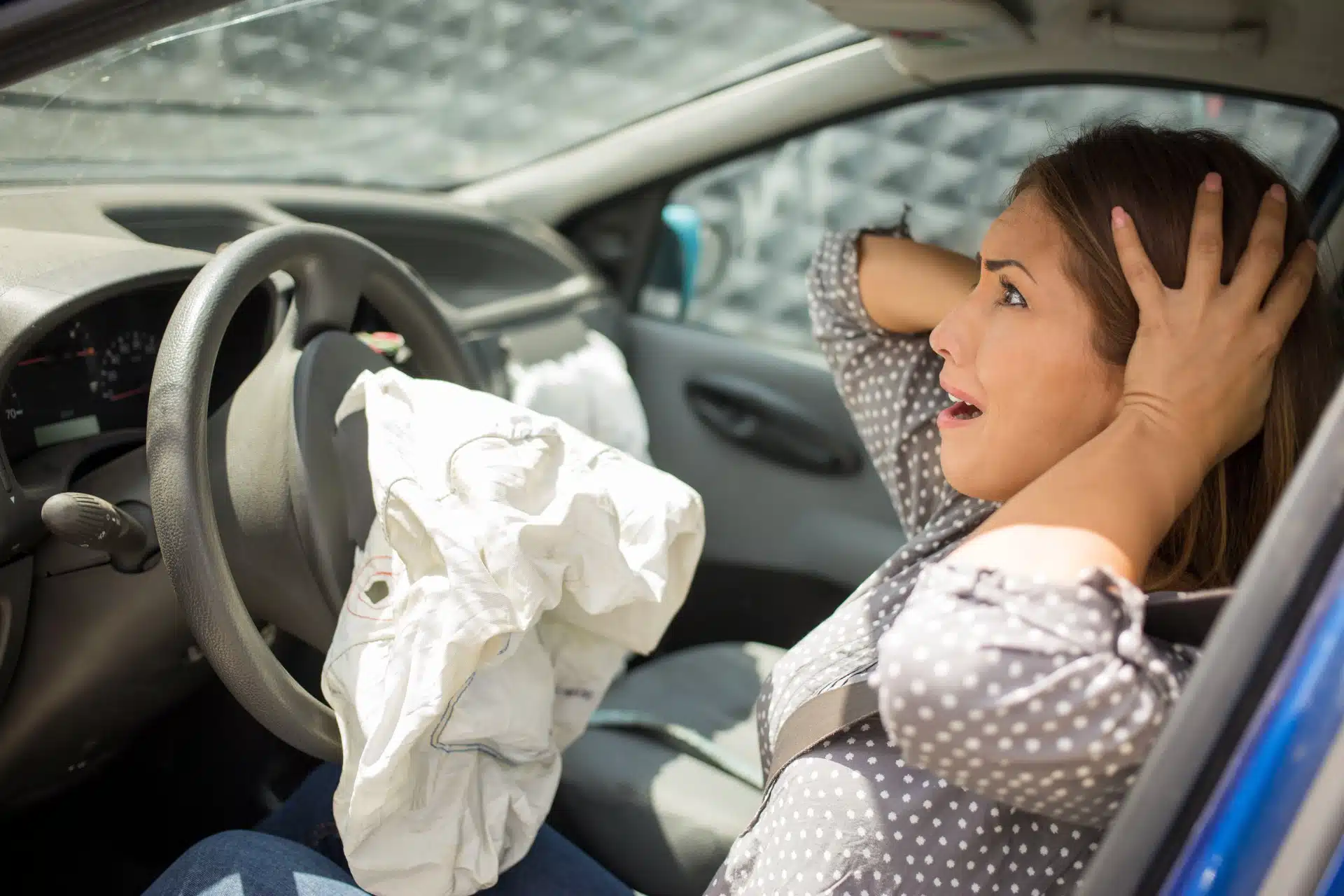 A woman holds her head while sitting in the driver's seat after an accident. The airbag has deployed - Takata airbag