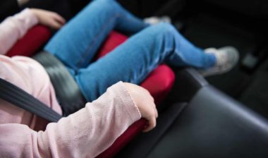 A child sits buckled into a car booster seat -