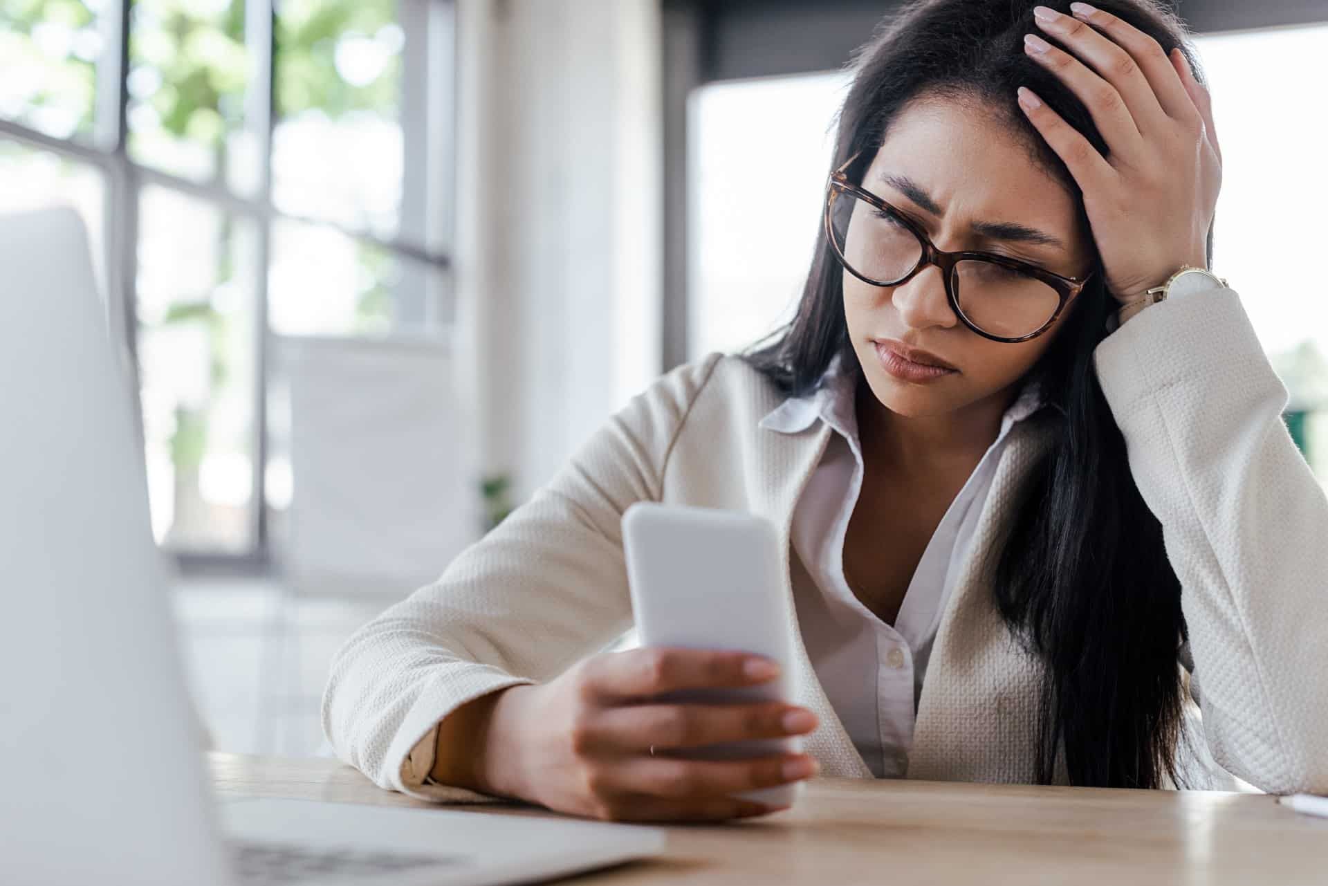 Frustrated woman sits with head in one hand while holding smartphone with the other - data throttling