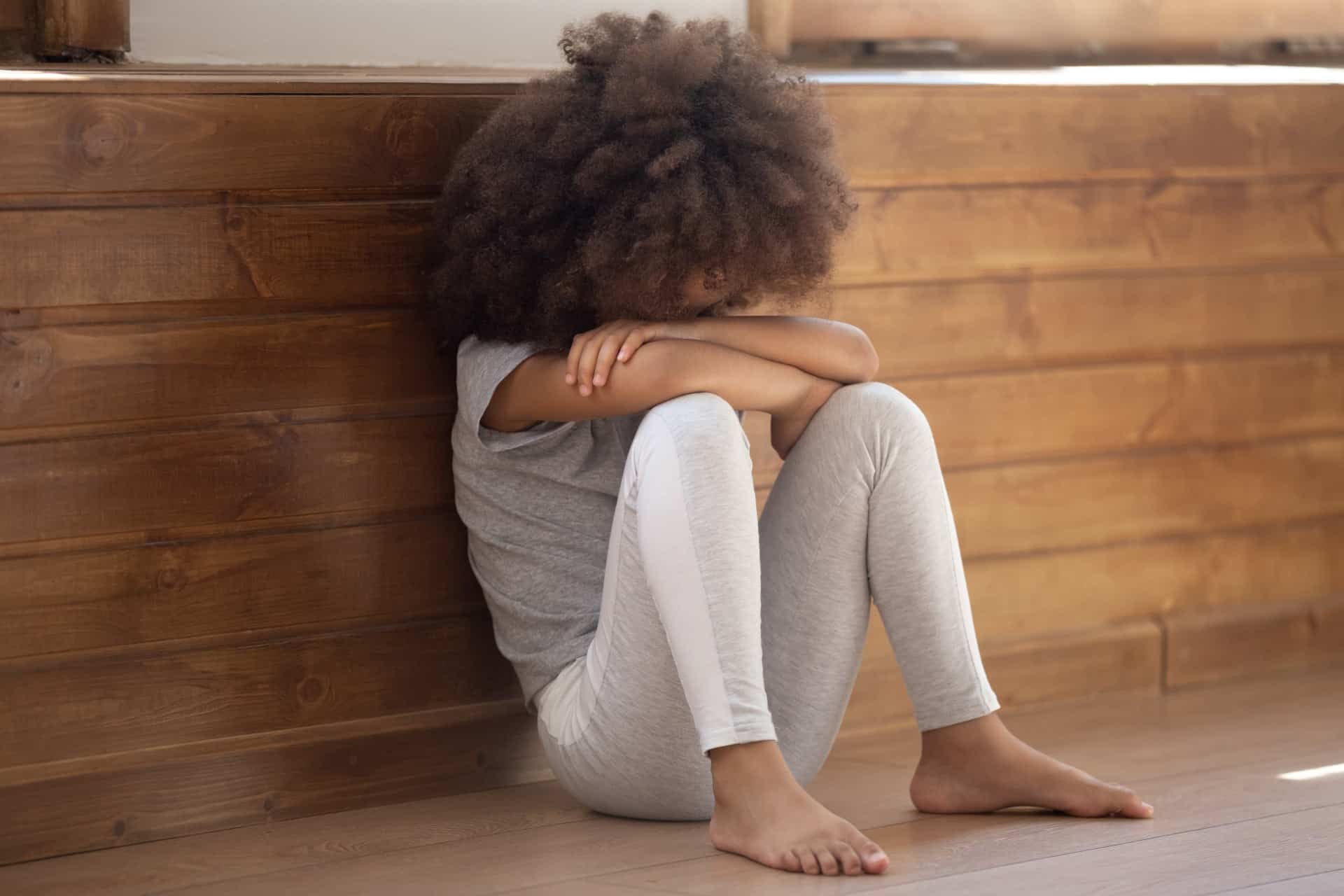 A girl hides her face in her arms resting on top of her knees - Boys and Girls Club of America