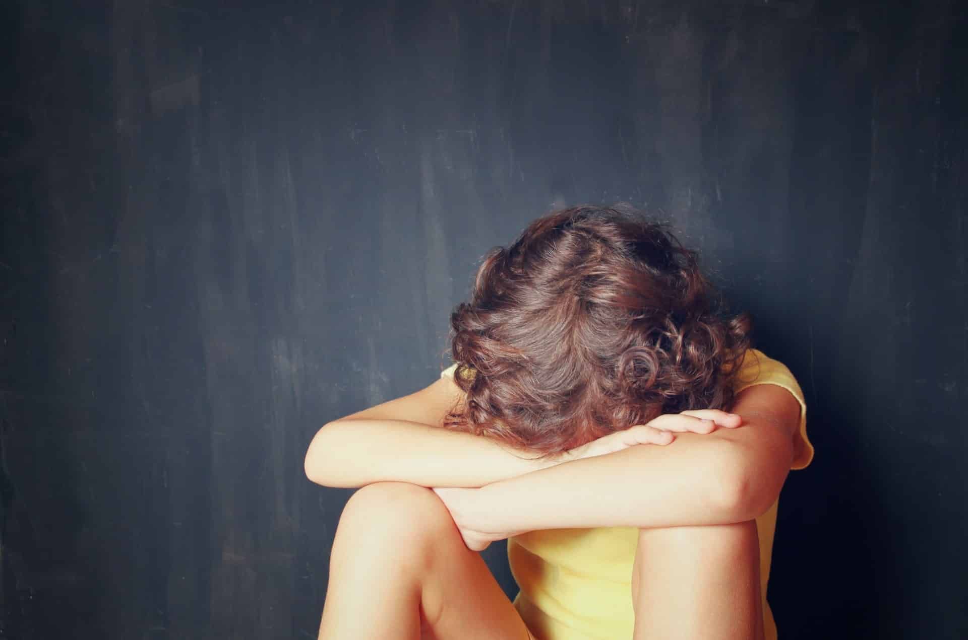 A child hides their face in their arms with their knees pulled to their chest - ymca
