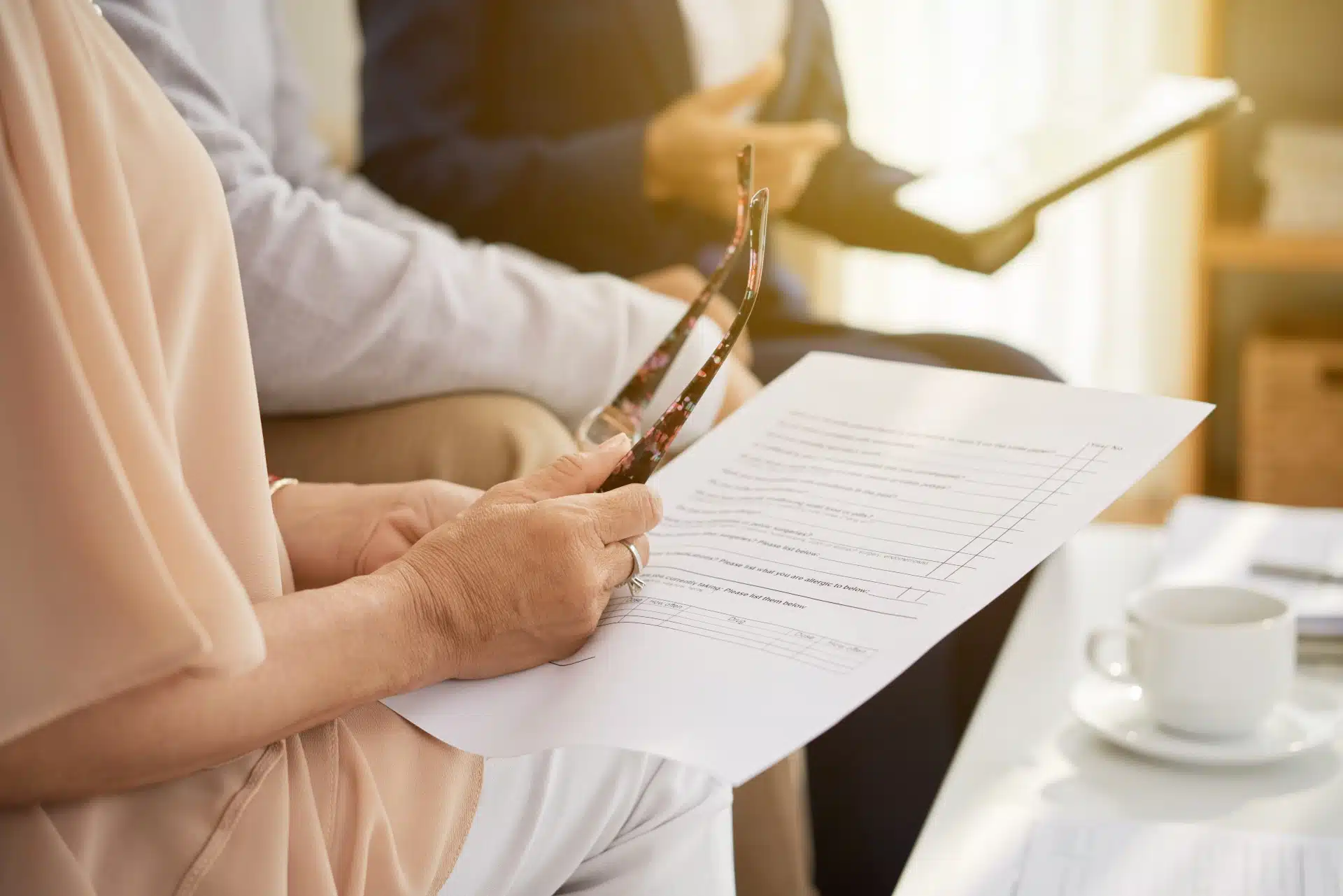 An insurance agent talks to a man and a woman holding a pair of glasses and a form - American General Life Insurance