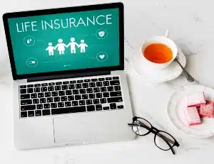 A laptop sitting next to a drink, cookies, and glasses, shows "life insurance" on the screen - American General Life Insurance