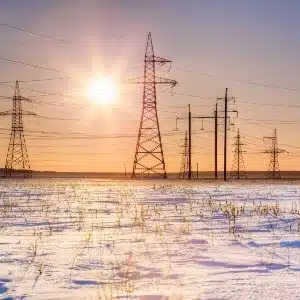 Snow on the ground near power lines, with the sun low in the sky - Texas electric grid failure