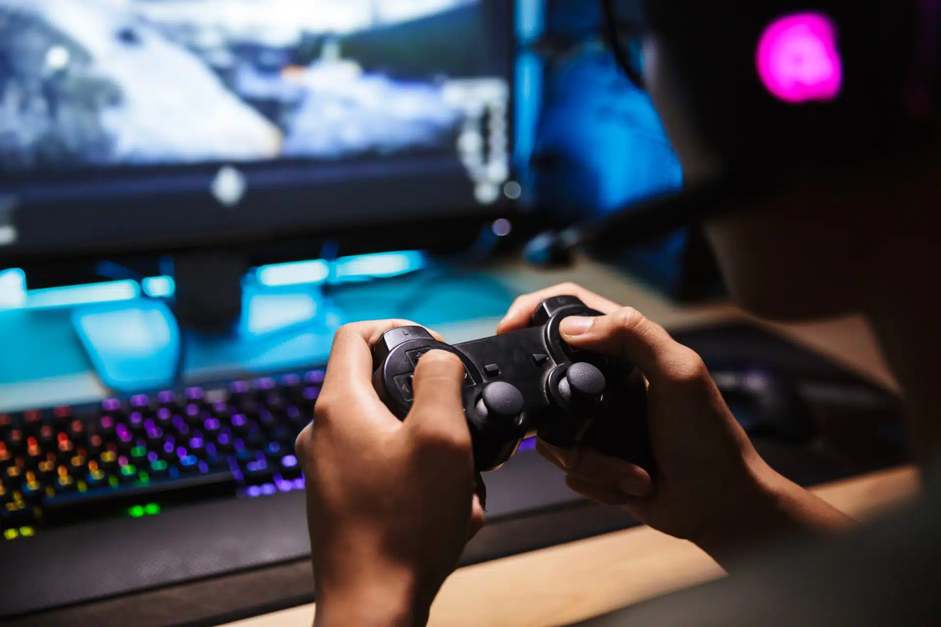 Closeup of hands holding a video game controller near a computer - Epic Games