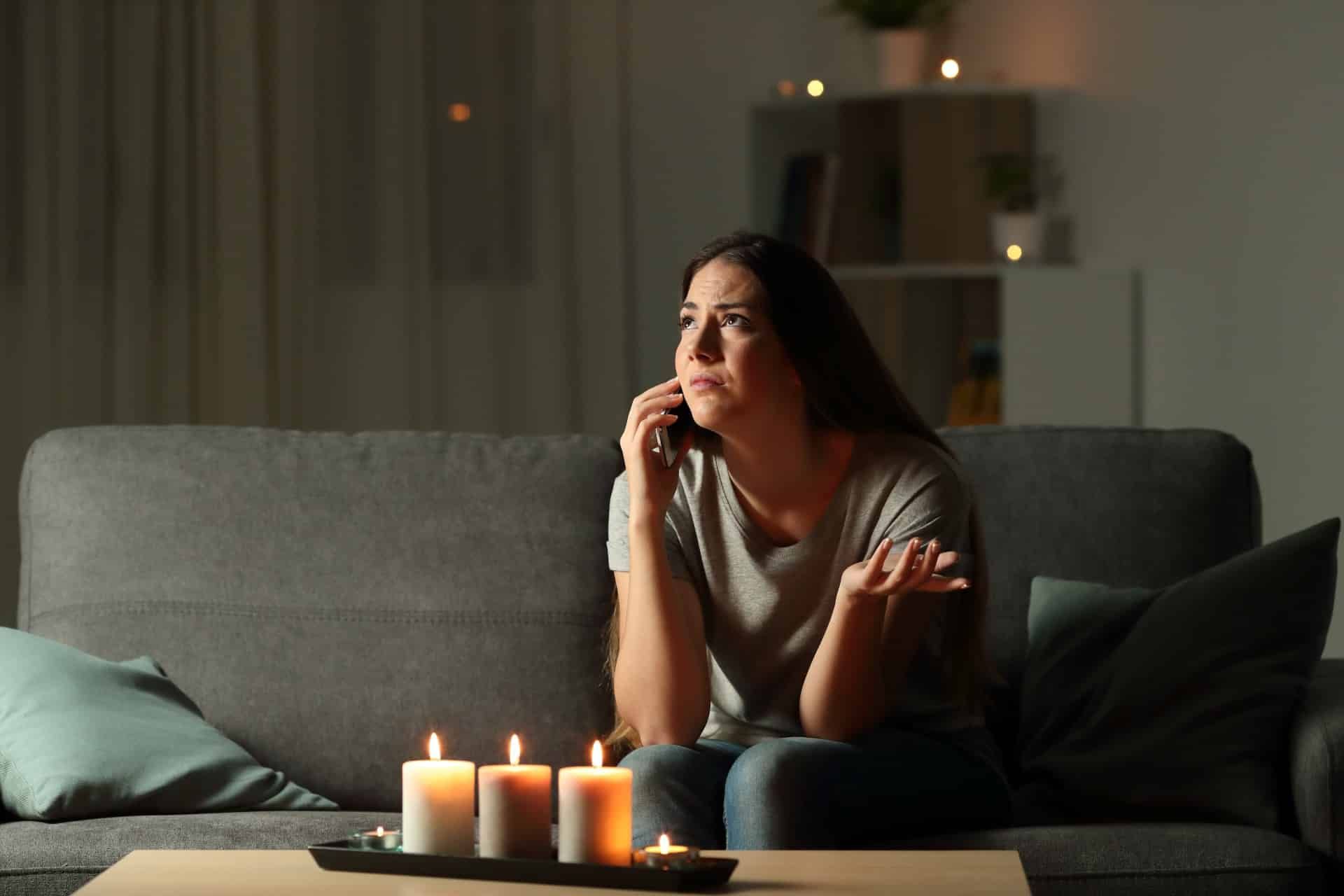 A woman in a power outage calls the electric company while sitting on her couch with candles around the room - texas power outage