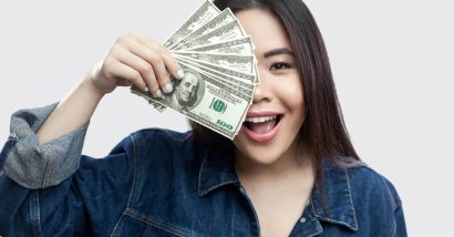 A happy Asian woman holds found out cash in front of half her face - class action settlement checks