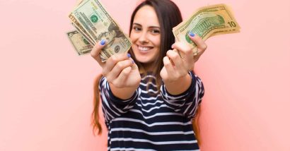 A woman in a striped shirt holds forward two hands full of cash - settlement checks