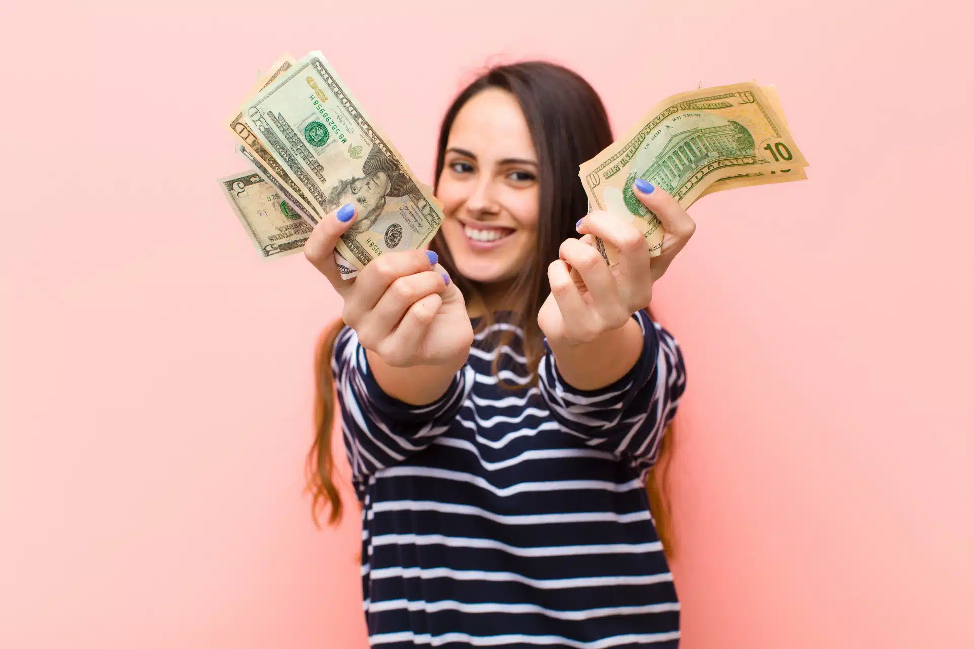 A woman in a striped shirt holds forward two hands full of cash - settlement checks