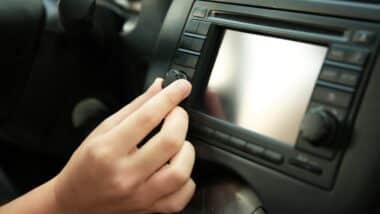 A driver's hand adjusts the volume on a car's infotainment system - GM