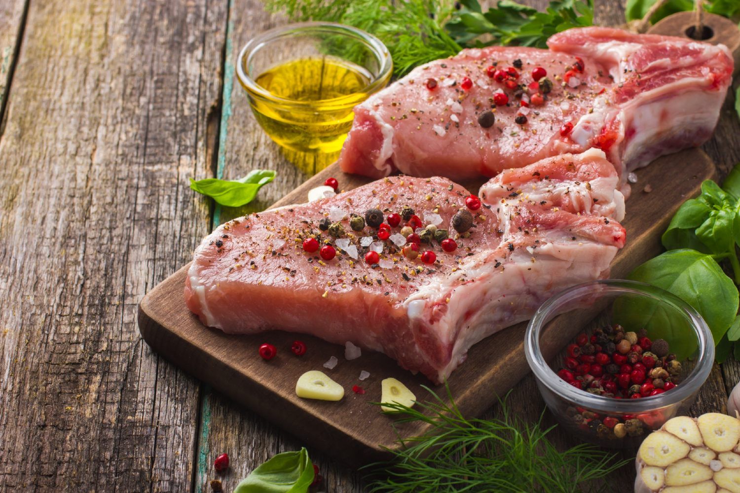 Dressed cuts of raw pork sit on a cutting board surrounded by other spices and oil - jbs usa