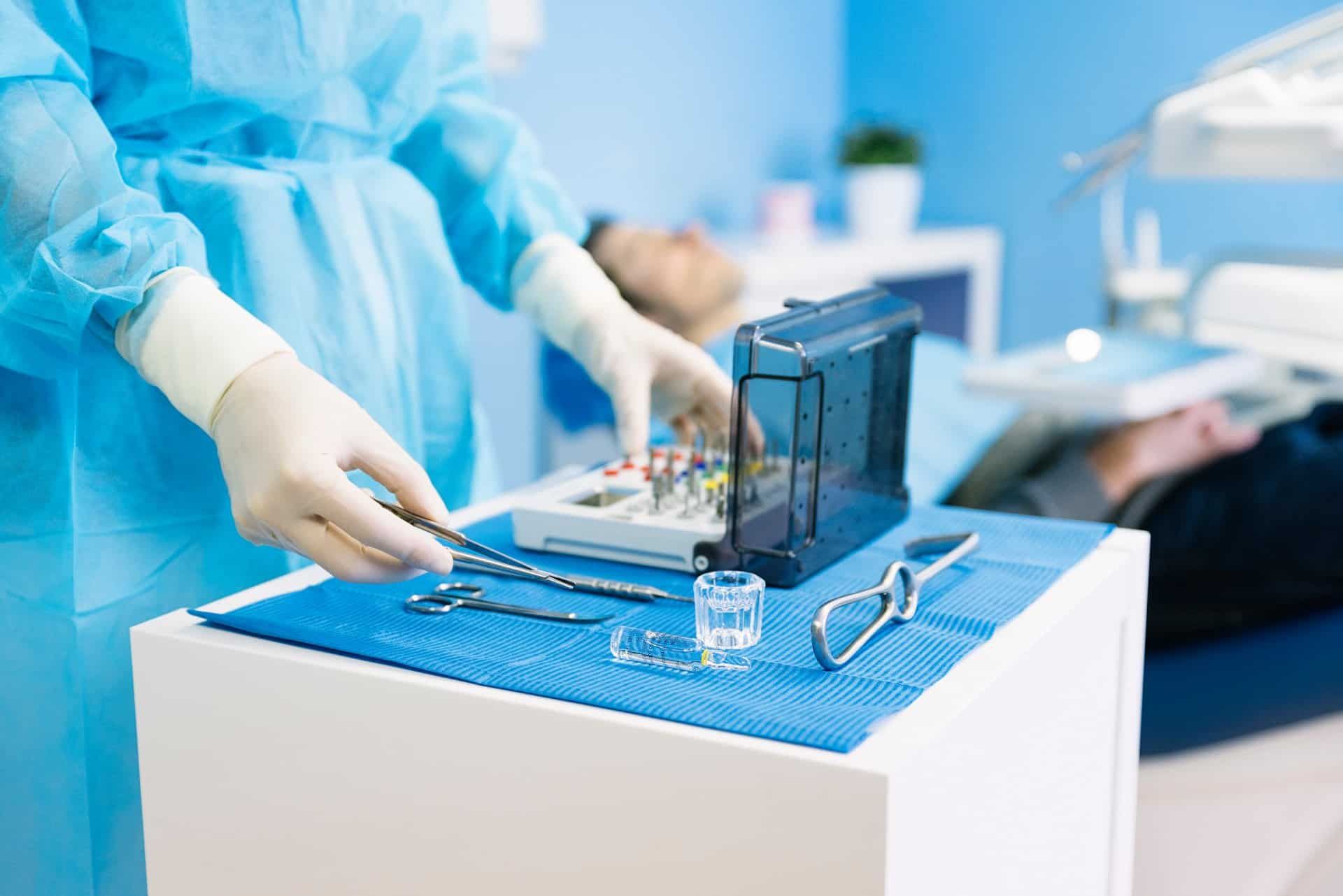 A dental tech handles tools while a patient waits in the background - nova southeastern university