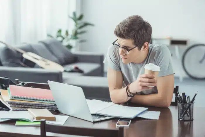 Male student with coffee and glasses studies on his laptop at home - tuition refund - SNHU - Southern New Hampshire University