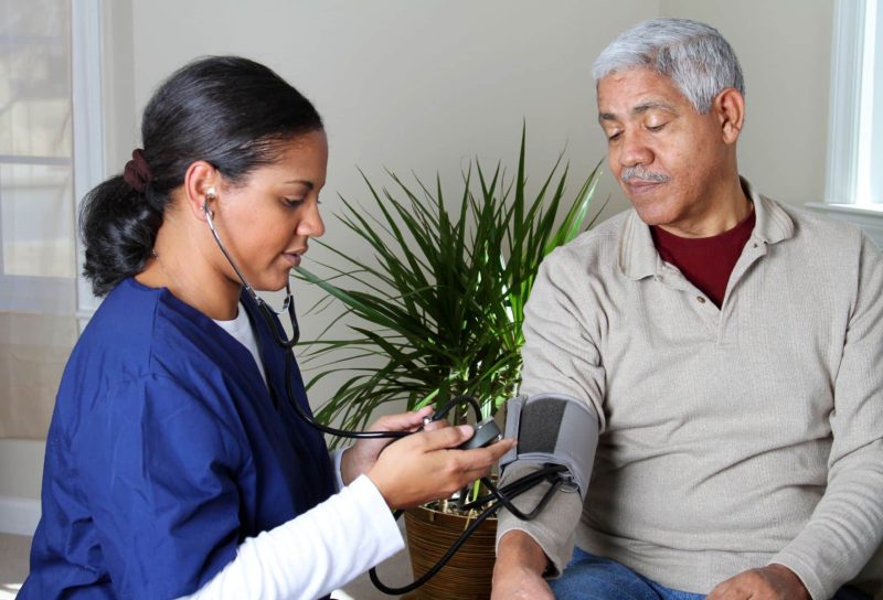 A home health care worker in dark blue scrubs takes an elderly man's blood pressure - humana home health