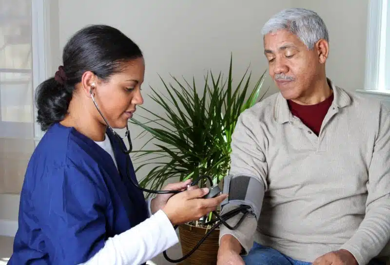 A home health care worker in dark blue scrubs takes an elderly man's blood pressure - humana home health