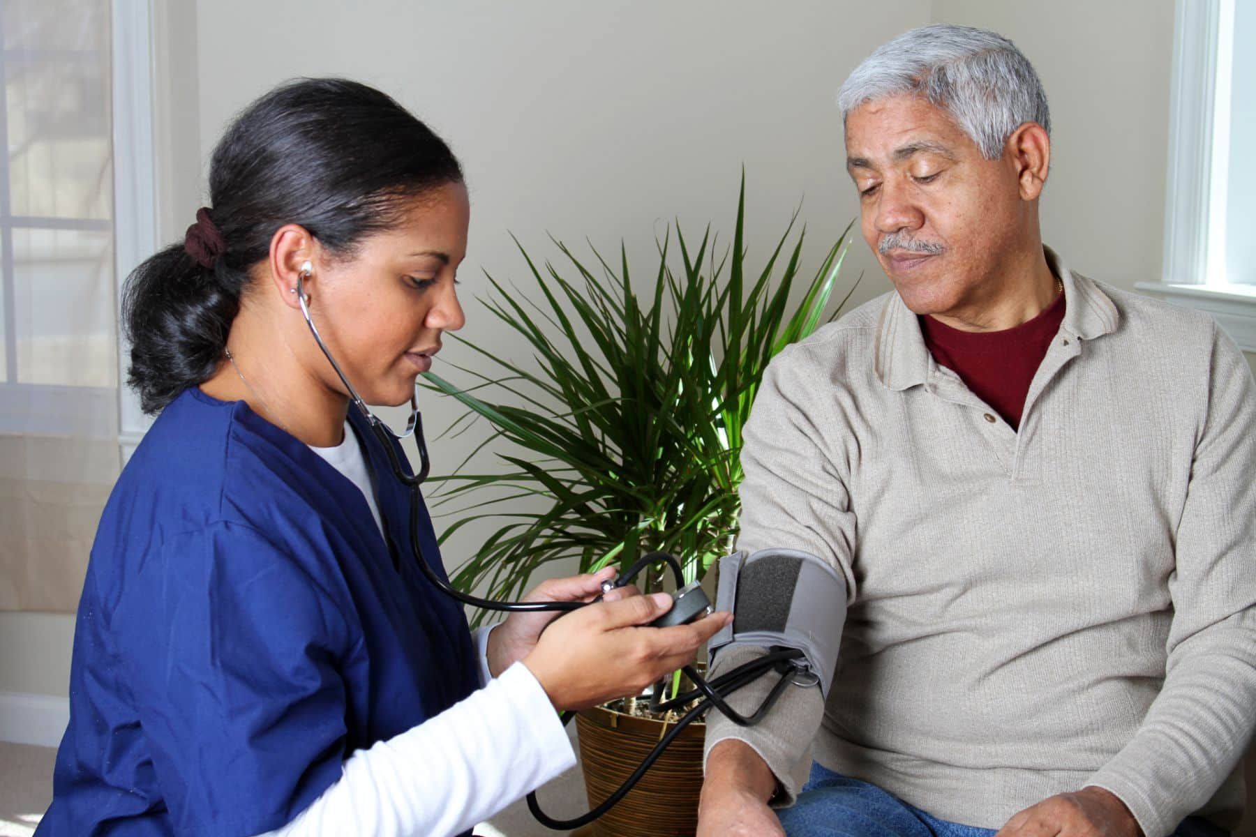 A home health care worker in dark blue scrubs takes an elderly man's blood pressure - humana home health