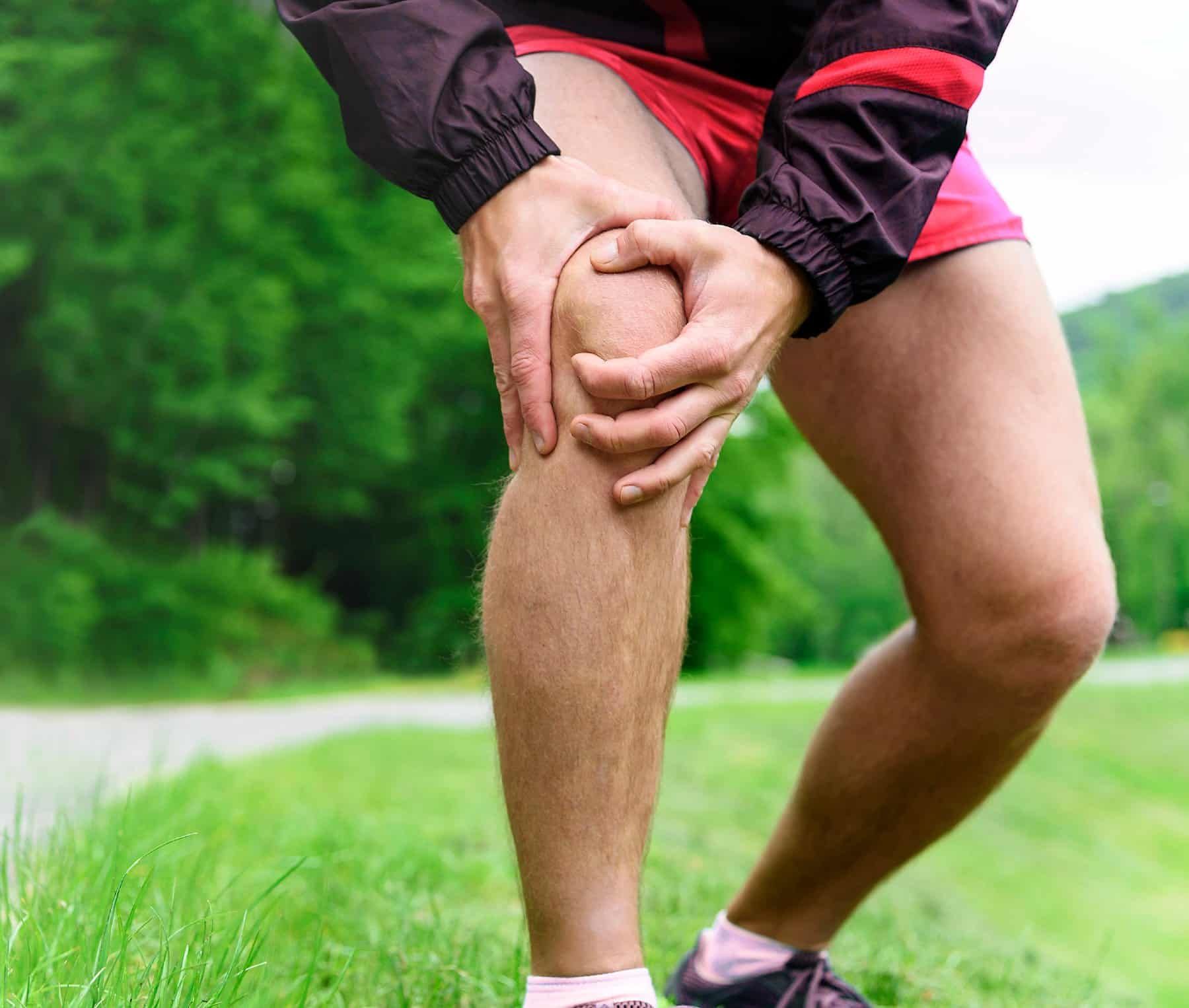 A runner grabs his knee in pain as he stands in the grass - spring valley glucosamine