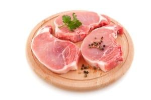 Raw pork chops with garnish on a circular wood cutting board - jbs usa