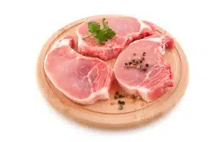 Raw pork chops with garnish on a circular wood cutting board - jbs usa