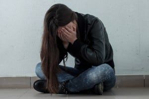 Sad teen girl sits cross-legged on the floor with her head in her hands - boys & girls club