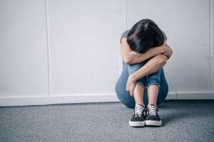Sad woman sits on the floor with her knees pulled to her chest and her head lying in her arm - james heaps lawsuits