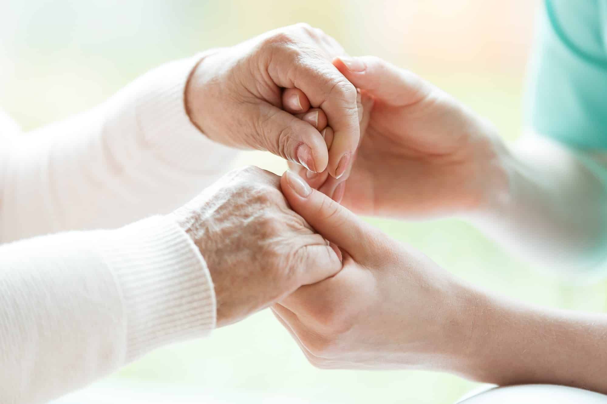 young hands holding older hands with arthritis