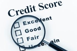 A magnifying glass lies on top of a paper that reads "Credit Score: Excellent Good Fair Uncertain" with checkboxes next to the options - First Advantage background check