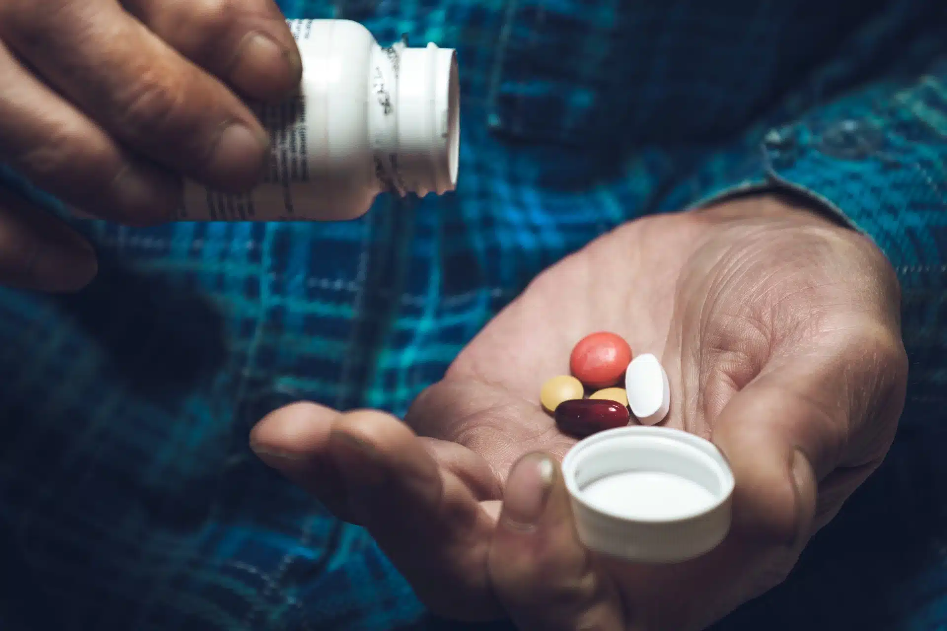 An elderly man pours a variety of pills into his hand from a white bottle - namenda