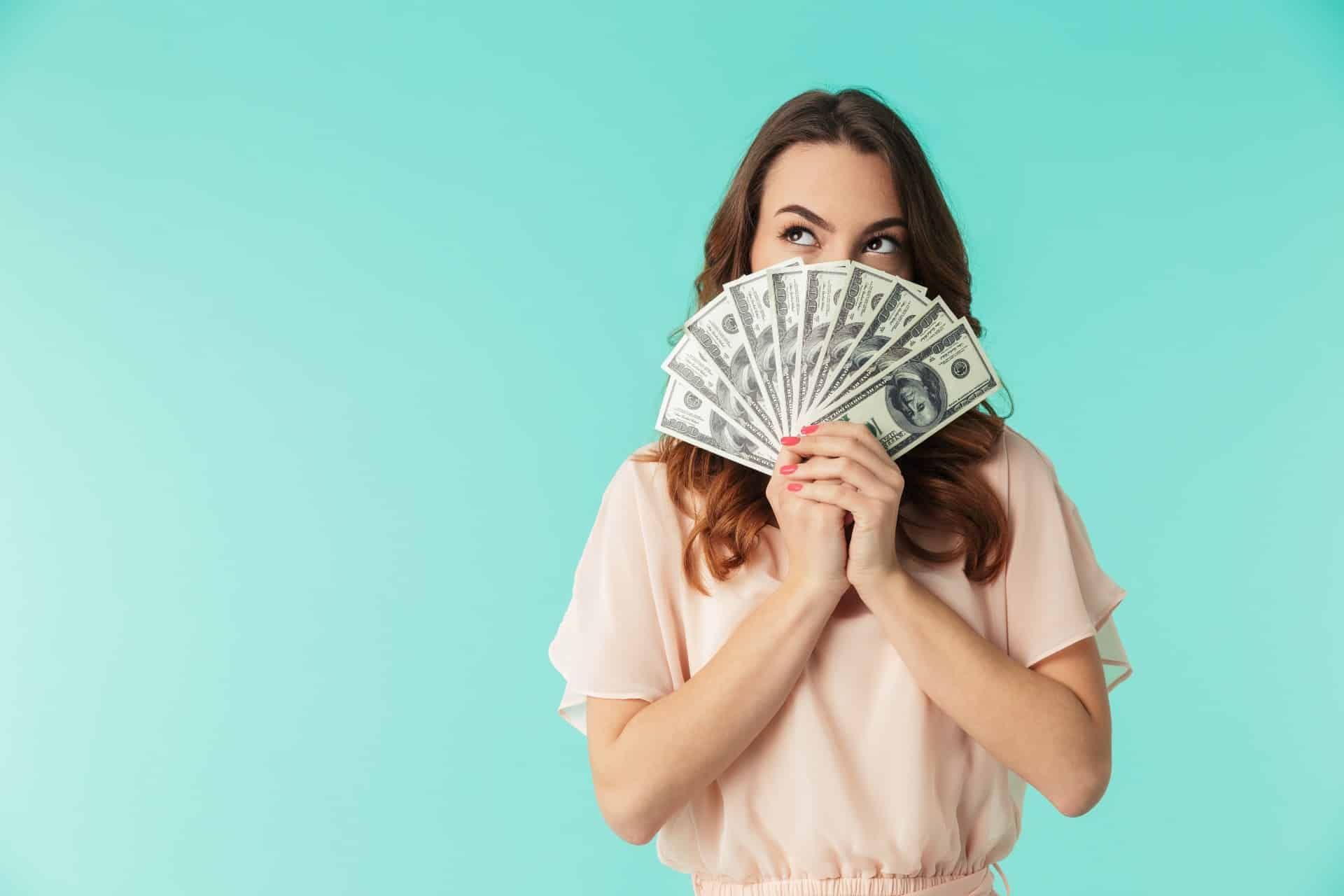 A dark-haired woman in a peach top holds fanned-out cash in front of the lower half of her face - settlement payout