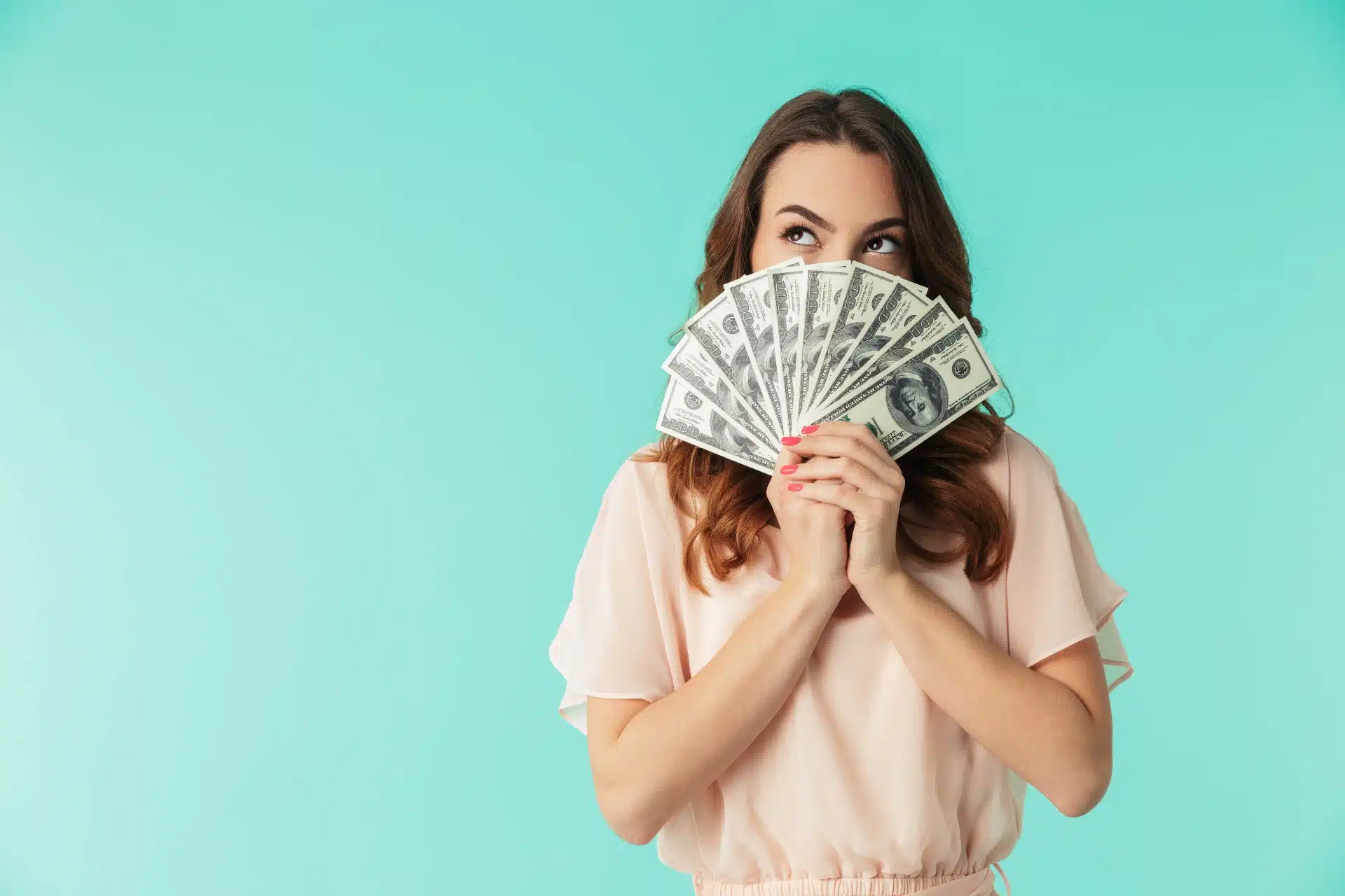 A dark-haired woman in a peach top holds fanned-out cash in front of the lower half of her face - settlement payout