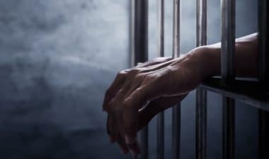 A pair of hands reaching through jail cell bars.