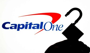 Capital One Bank logo on the screen in a main focus and a blurred silhouette of the open lock. Conceptual photo for news about the bank data breach.