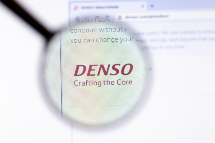 Denso logo is seen on a computer screen under a magnifying glass - instrument panel clusters - denso auto parts - denso lawsuit - auto parts class action