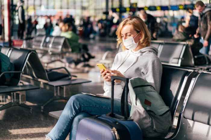 A masked traveler in an airport scrolling through a cell phone.