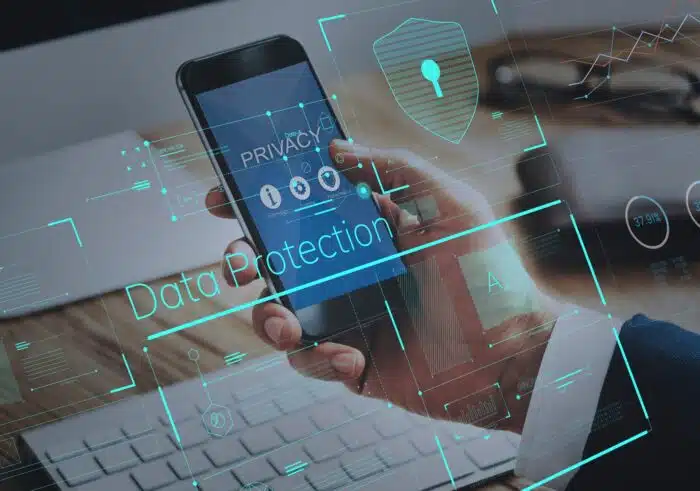 A man's hand holds a smartphone near a computer; a "data protection" graphic is overlaid - plaid data