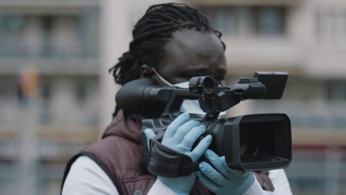 Close up, african black videographer with medical mask looking through the viewfinder on video camera
