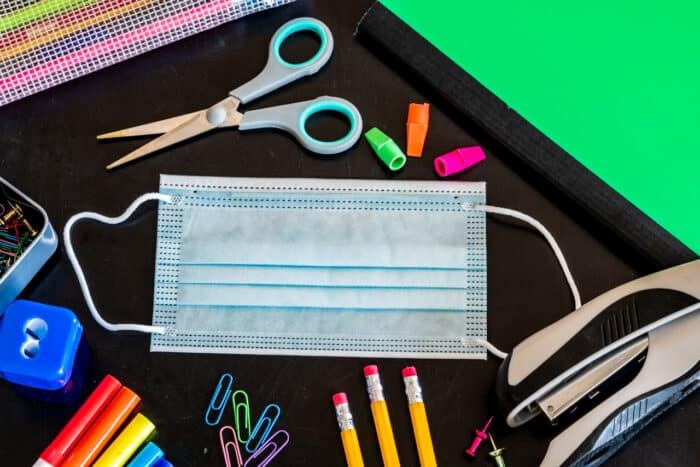 A mask with grade school supplies on a dark chalkboard background.