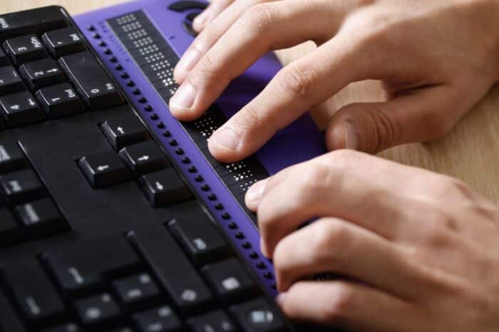 Blind person using computer with braille computer display and a computer keyboard. Pure Romance, website, ADA, class action.