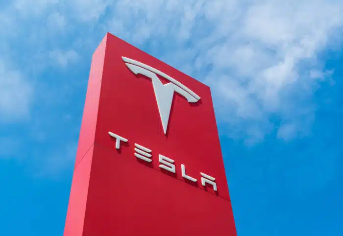 The Red Tesla Motors sign rising up into blue sky with a few clouds