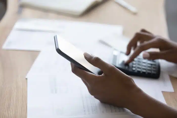 Close up young african american biracial woman holding smartphone in hands, calculating domestic expenses - telephone payments - mortgage payment - roundpoint mortgage settlement
