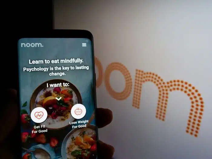 Person holding mobile phone with website of US weight-loss platform company Noom Inc. on screen in front of logo.