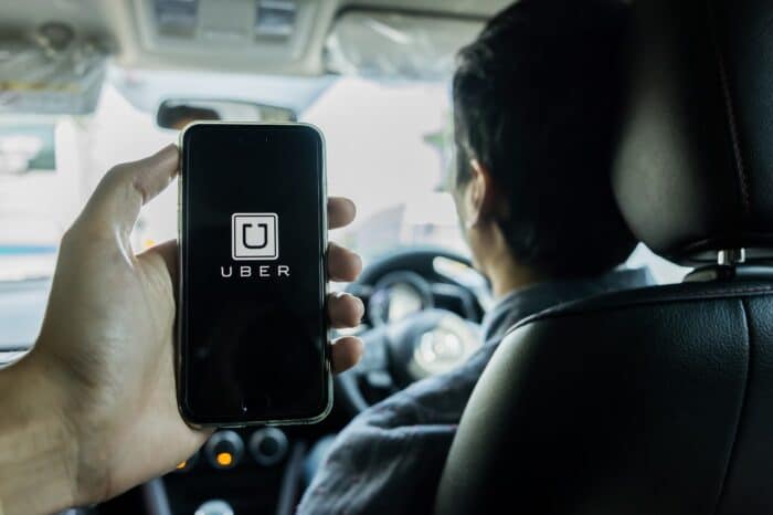 A man hand holding Uber app showing on iPhone 6s on road and black car,