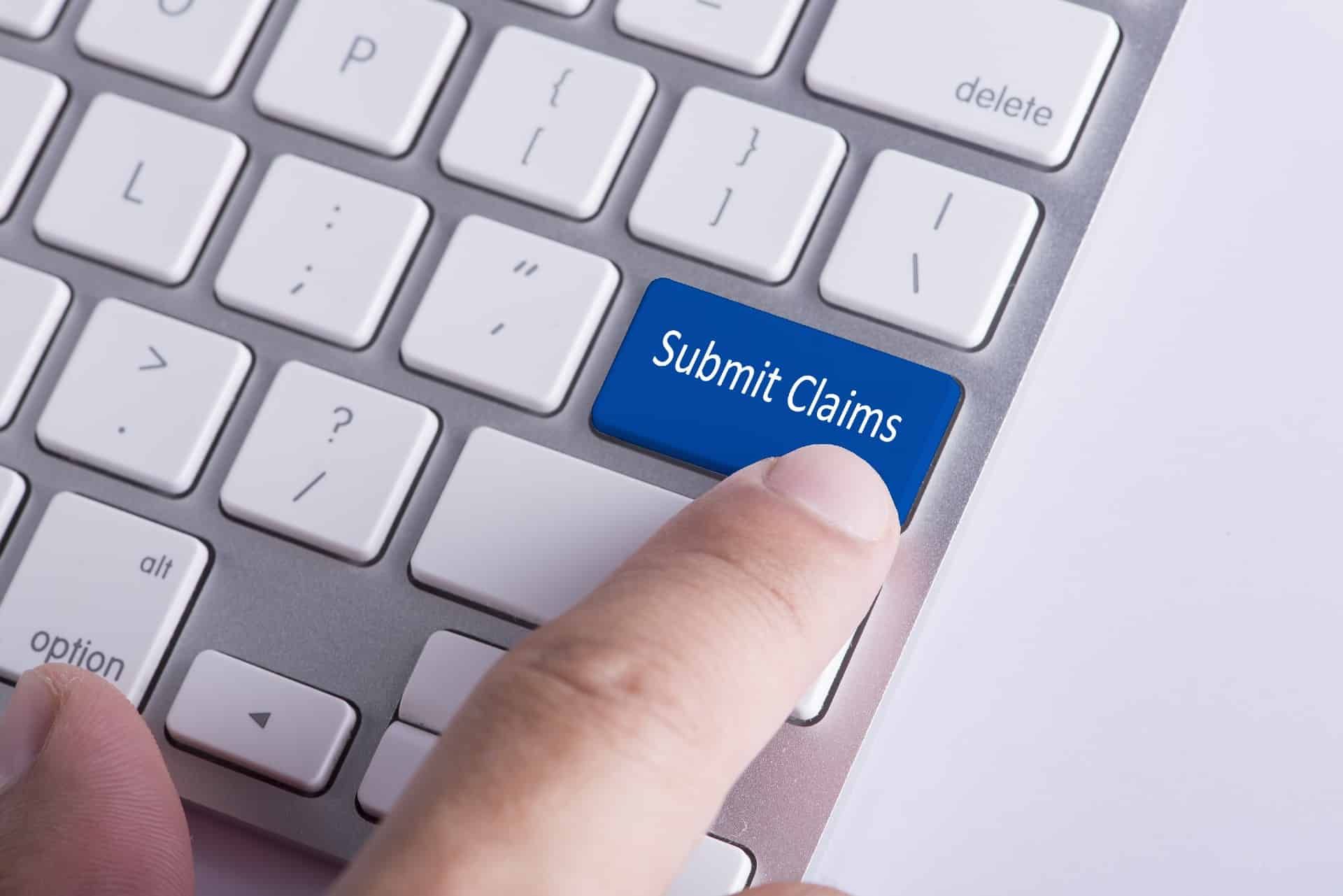 A person pushes a blue "submit claim" button on a computer keyboard - settlements closing