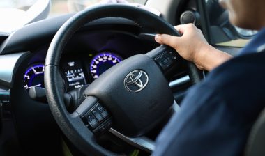 Toyota steering wheel with driver’s hands hold it.